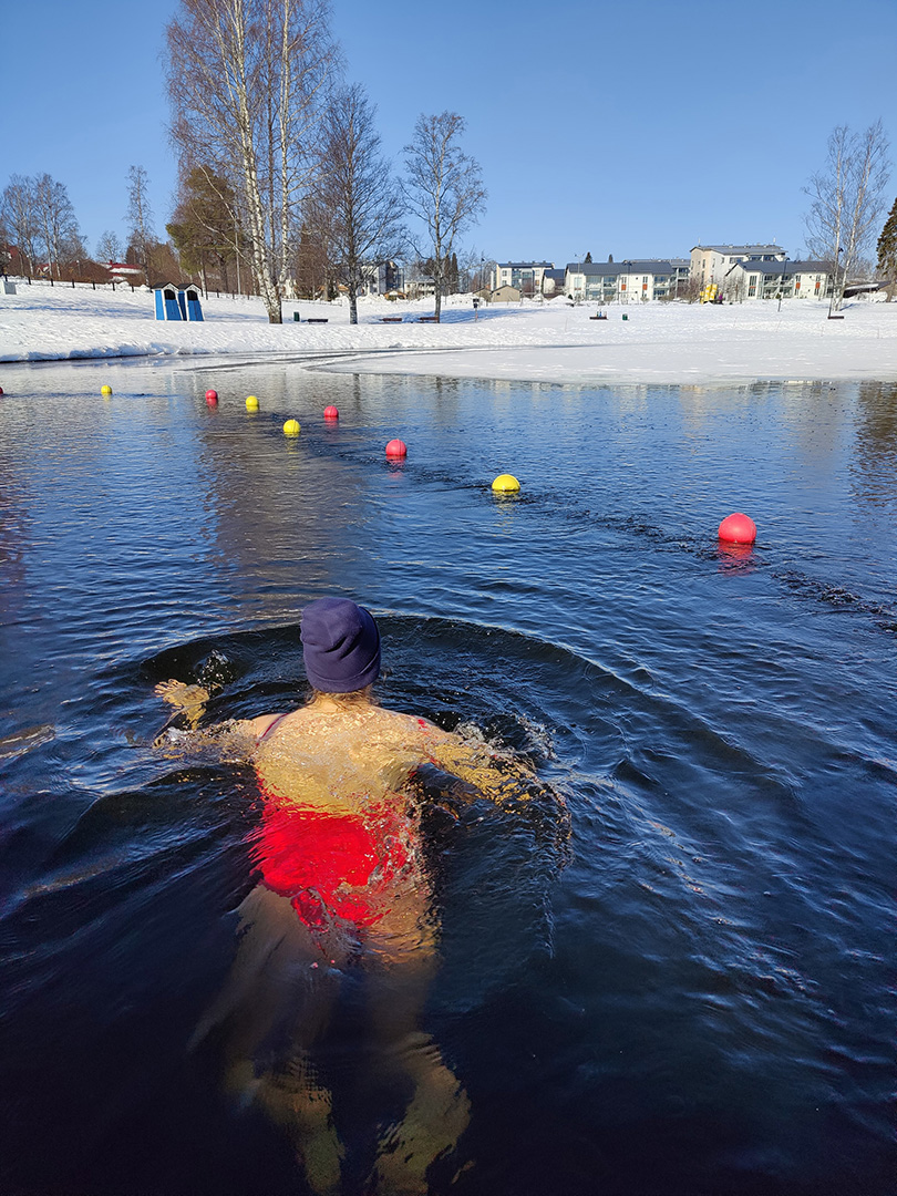 Henkilö uimassa järvessä talvella.